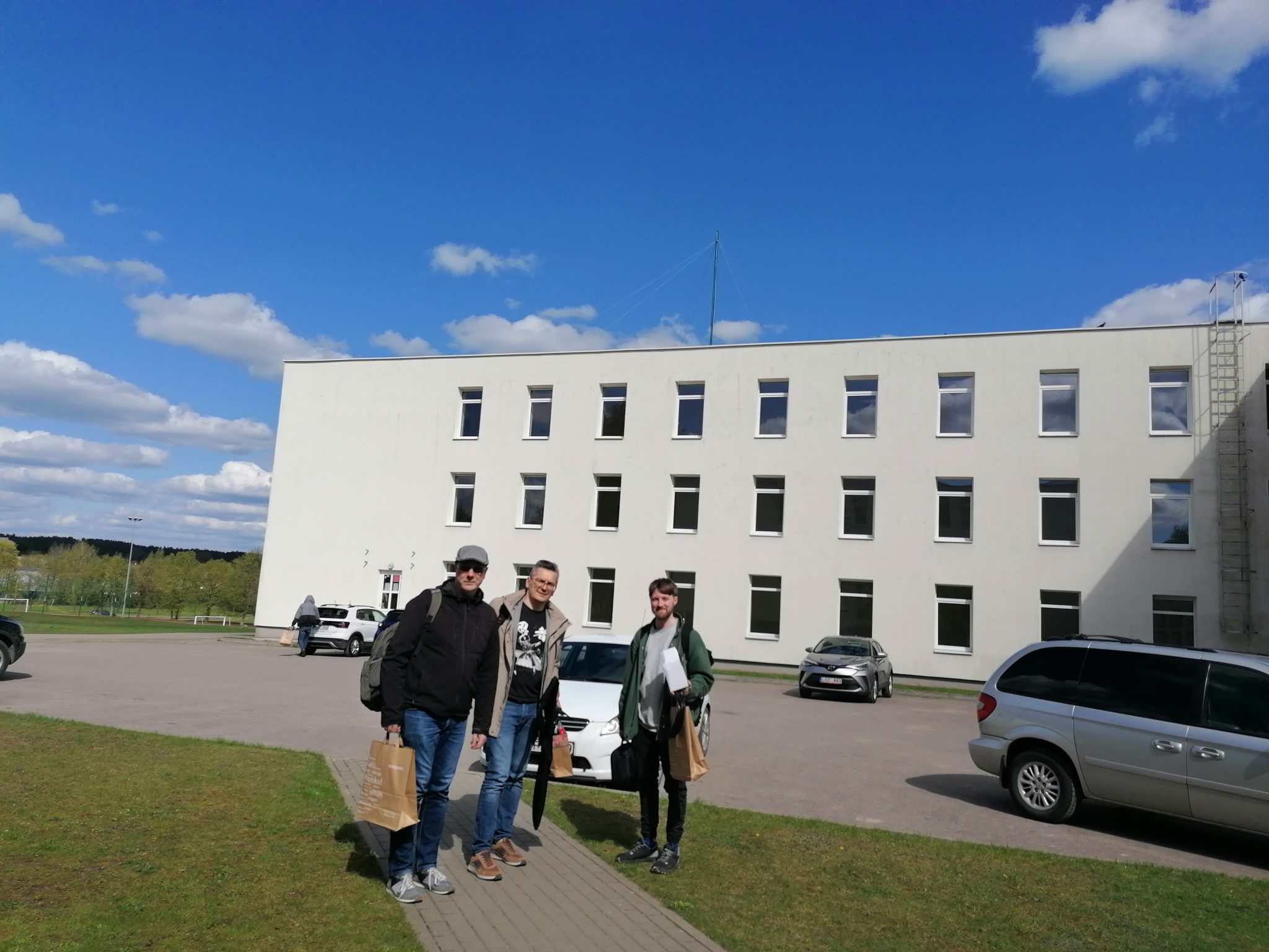 Vilniaus universiteto radijo klubo komanda stovi prie mokyklos, fone ant stogo matosi iškeltas stiebas